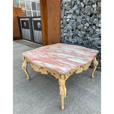 an old pink and gold coffee table sitting in front of a pile of rocks