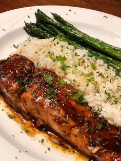 a white plate topped with meat and rice covered in sauce next to asparagus