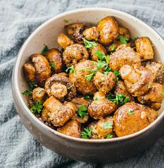 a white bowl filled with cooked potatoes and parsley on top of a blue towel