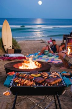 people are sitting on the beach near an open fire pit with grills and surfboards