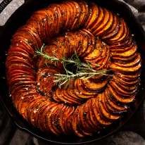 cooked sweet potatoes in a cast iron skillet with rosemary sprigs on top