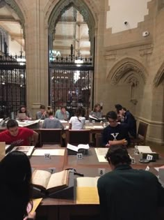 several people sitting at tables with books in front of them and an iron gate behind them