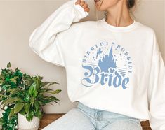 a woman sitting on a bench wearing a white sweatshirt with the words bridal printed on it