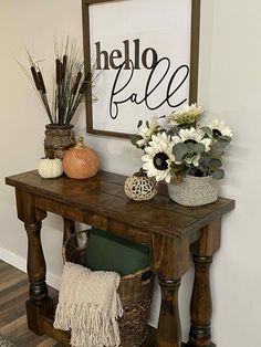 a wooden table topped with vases filled with white flowers and plants next to a sign that says hello fall