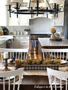 a kitchen filled with lots of white furniture and lights hanging from the ceiling above it