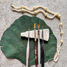 a bunch of paint brushes sitting on top of a green leaf next to some beads