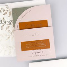 two folded wedding cards on top of each other next to an envelope with gold foil