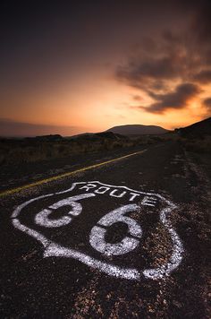 a road sign on the side of an empty road at sunset with clouds in the sky