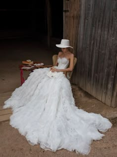 a woman sitting in a chair wearing a white dress and hat with feathers on it