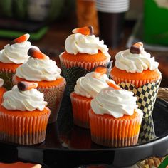 cupcakes with white frosting and orange icing are on a black plate