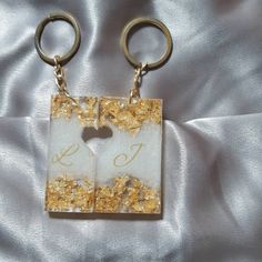 two gold and white square keychains with initials on them