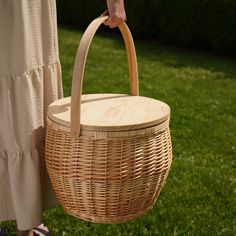 a person holding a wicker basket in their hand on the grass with trees in the background