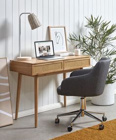 a desk with a chair and pictures on it in front of a wall mounted plant