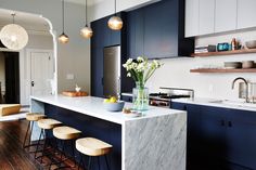 a kitchen with blue cabinets and marble counter tops, stools at the bar area