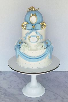 a three tiered cake with blue and gold decorations on it's side, sitting on a white pedestal