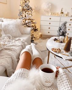 a woman in white sweater and leg warmers holding a cup of coffee while sitting on a couch