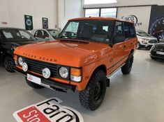 an orange land rover is parked in a showroom with other cars around the room