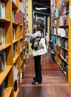 a woman is standing in the middle of a library holding a bag and looking at books