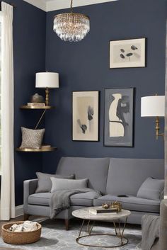 a living room with blue walls and grey couches, chandelier hanging from the ceiling