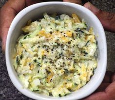 a person holding a white bowl filled with food on top of a stone countertop