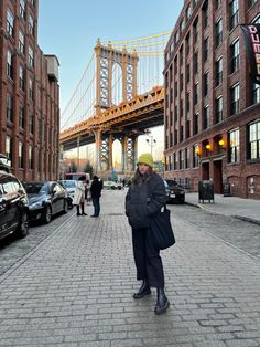 a woman standing in the middle of a brick road near tall buildings and a bridge