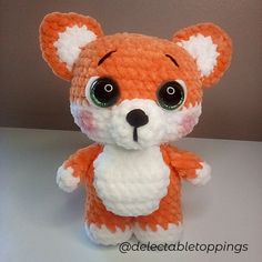 an orange and white crocheted stuffed animal with big eyes sitting on a table