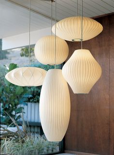 three white lamps hanging from the ceiling in front of a wooden door and planters