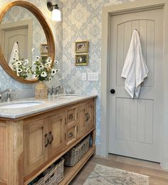 a bathroom with blue wallpaper and wooden cabinetry, mirror over the sink, and white towels hanging on the door