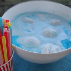 a bowl filled with blue liquid next to some straws