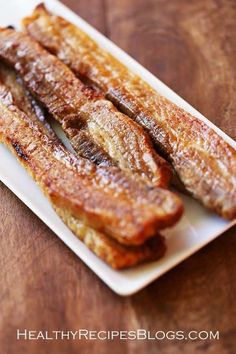 some bacon is on a white plate on a wooden table and it looks like they have been cooked in the oven