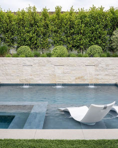 an outdoor swimming pool with artificial grass and water features, including two white lounge chairs