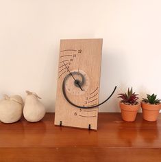 a wooden clock sitting on top of a table next to potted plants and two small pots