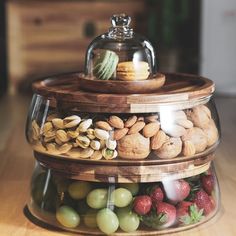 three tiered glass container filled with nuts, grapes and almonds on top of a wooden table