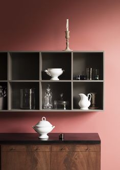 an empty shelf with vases and other items on it in front of a pink wall