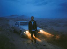 a man standing next to a car in the middle of a dirt road at night