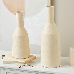 two white vases sitting on top of a table next to a book and candle