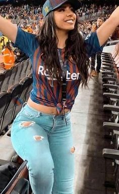 a woman is standing in the stands at a baseball game wearing ripped jeans and a hat