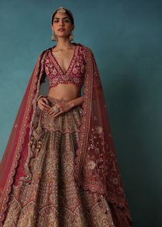 a woman in a red and gold lehenga is standing with her hands on her hips