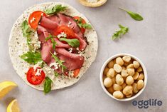 a tortilla with meat, tomatoes and lettuce next to a bowl of chickpeas