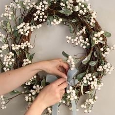 someone is making a wreath with white flowers and greenery