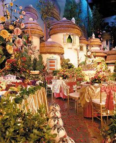 a room filled with lots of tables and chairs covered in white cloths next to plants