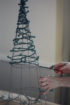 two hands are decorating a wire christmas tree