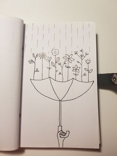 an open notebook with a drawing of flowers and a person holding an umbrella in the rain