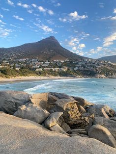 the beach is full of rocks and people are swimming in the water near the mountains