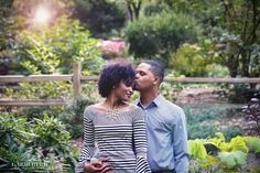 a man and woman standing next to each other in front of some bushes with trees