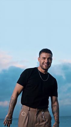 a man standing in front of the ocean with his hands on his hips and smiling