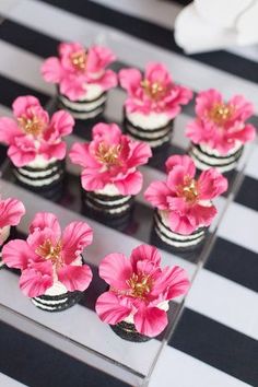 cupcakes decorated with pink flowers are on a black and white striped tablecloth