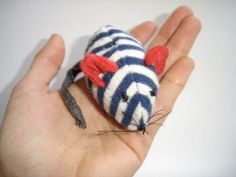 a hand holding a small stuffed animal in it's left palm, with red and white stripes on its body