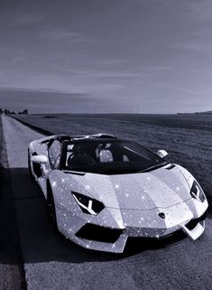 a white sports car parked on the side of a road next to an empty field