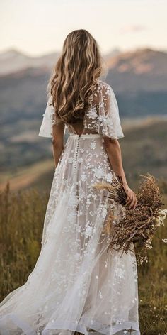 a woman in a white dress standing on top of a grass covered hill with her back to the camera